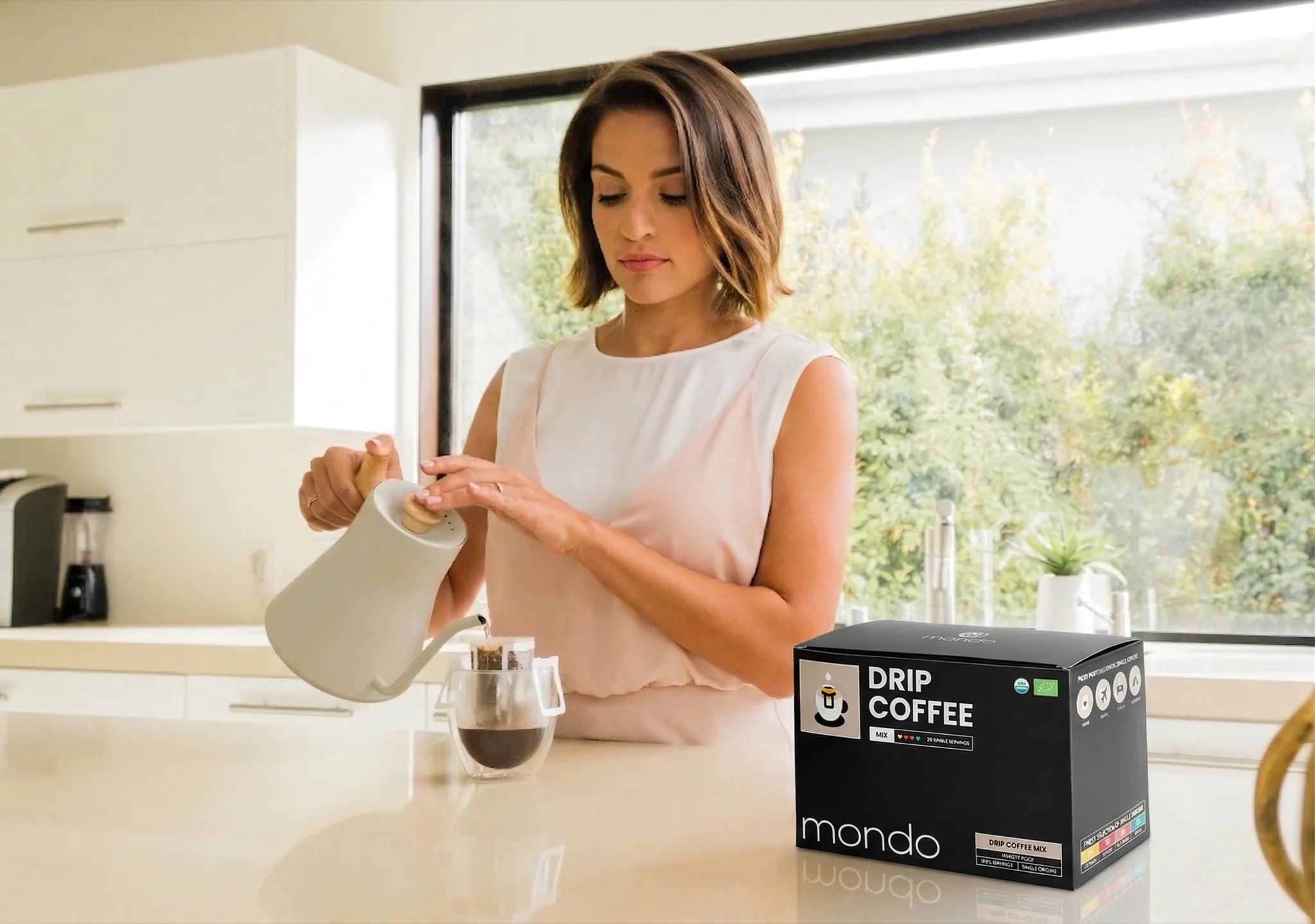 Woman preparing coffee in a kitchen with a Mondo coffee box on the counter.